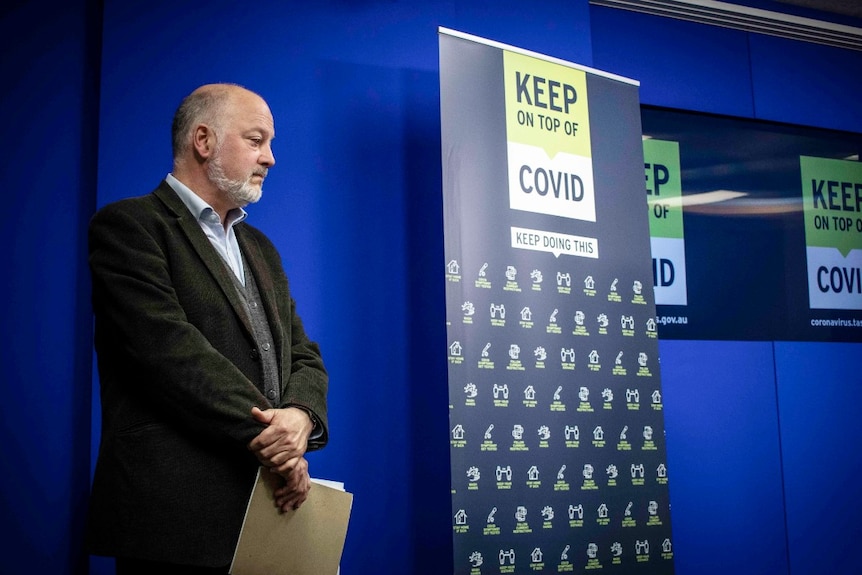 A man stands next to a sign reading Keep on top of COVID