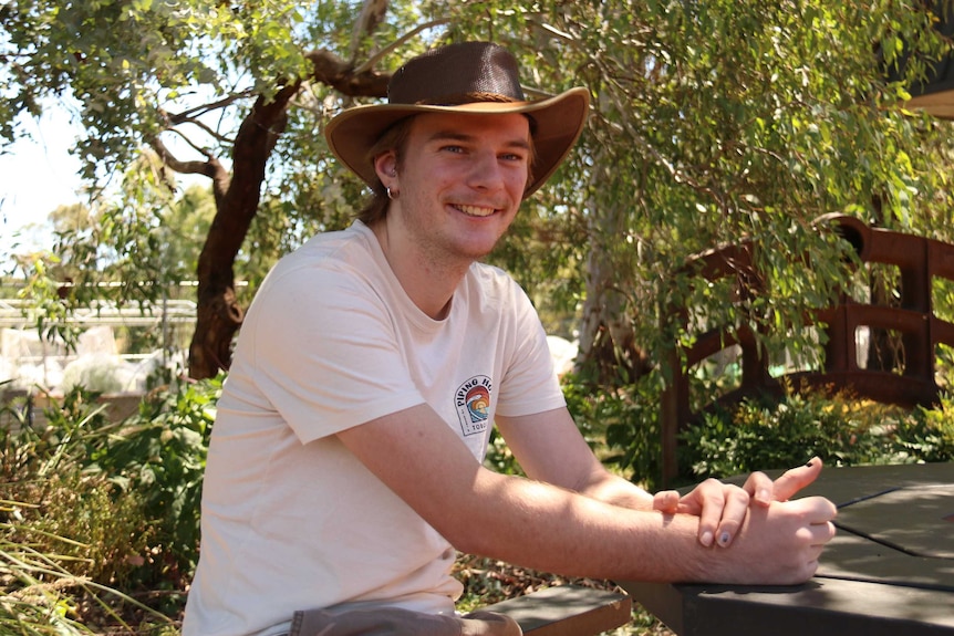 A young man in an Akubra leans on a table.