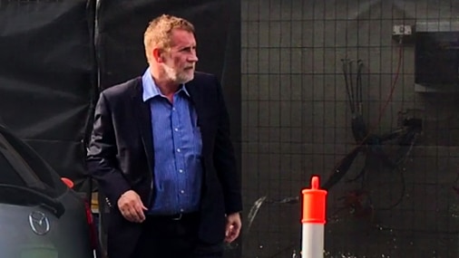 Philip Whiteman, with suit, blue shirt, and brown hair, standing on a suburban street.