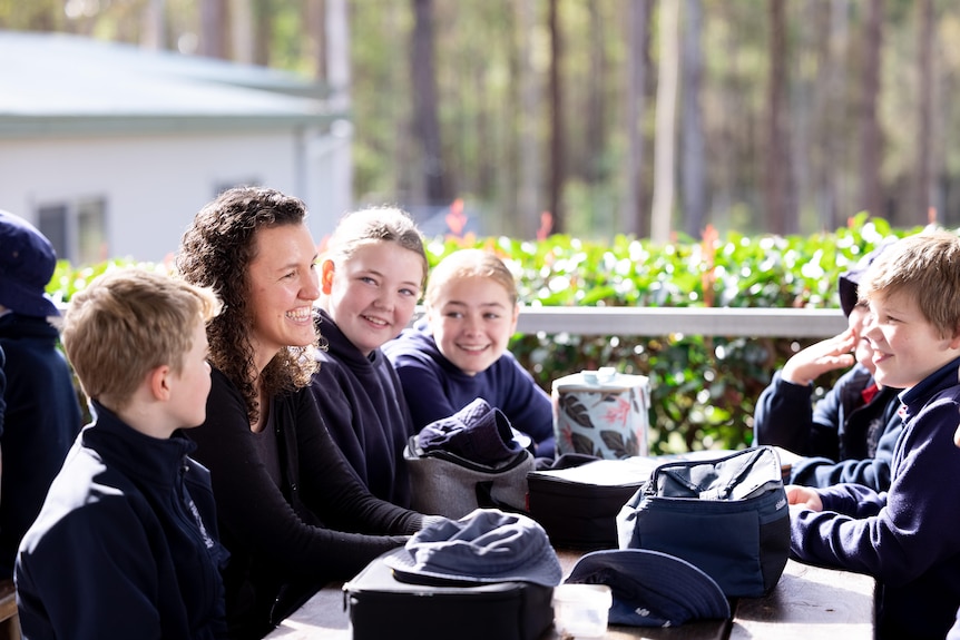 A teacher sits at a table with a group of primary school students.