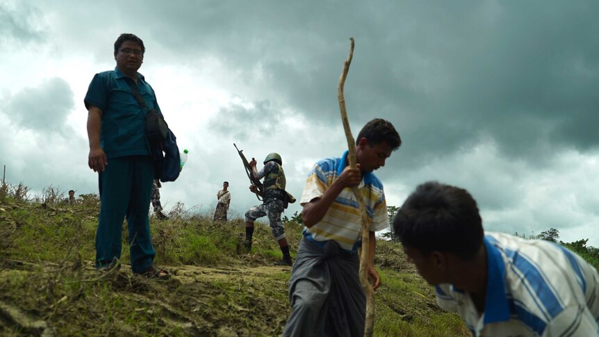Two men work in a field as soldiers walk past in Rakhine region of Myanmar.