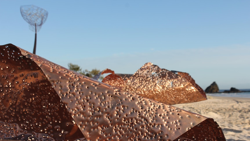 Sculpture on a beach made from copper sheets with shotgun pellet holes.