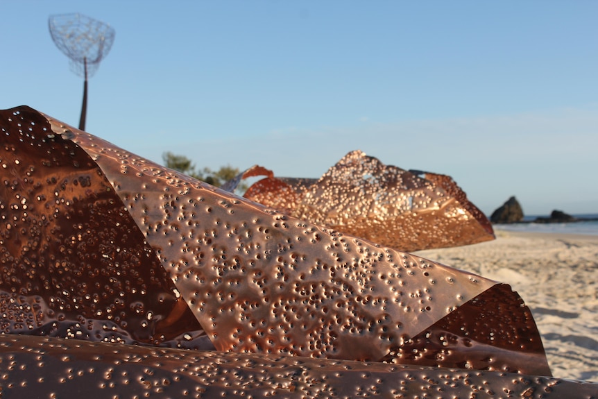 Sculpture on a beach made from copper sheets with shotgun pellet holes.