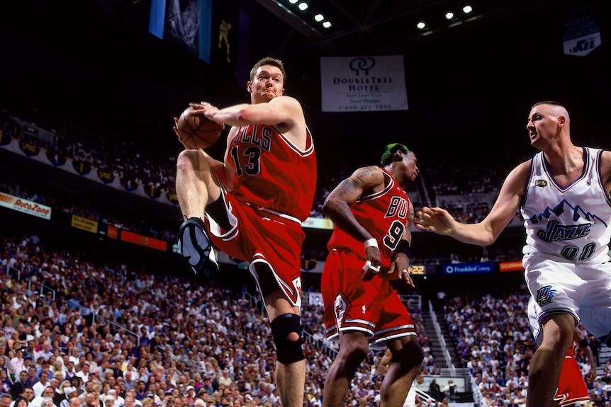 Bulls number 13 Luc Longley lifts his leg in action on the court as a Jazz player approaches
