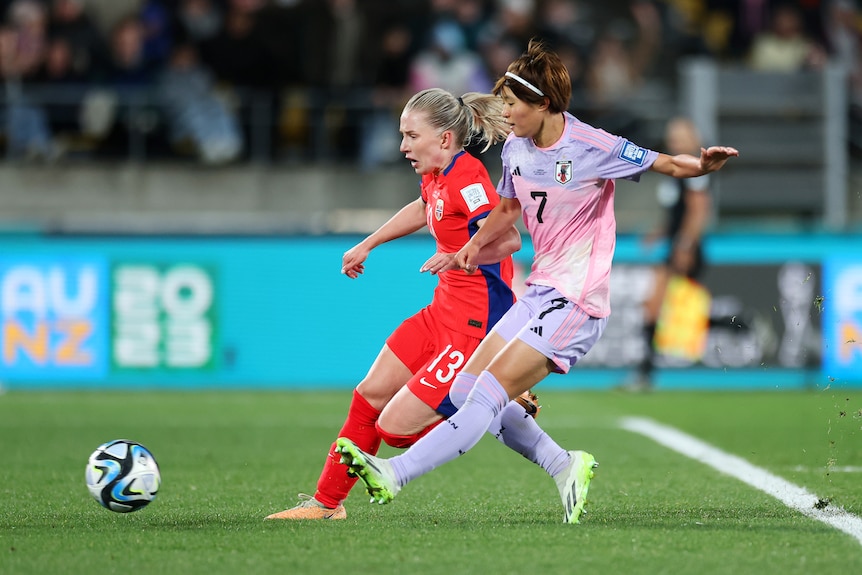 A Japanese striker sidefoots the ball towards goal as she runs alongside a Norway defender.
