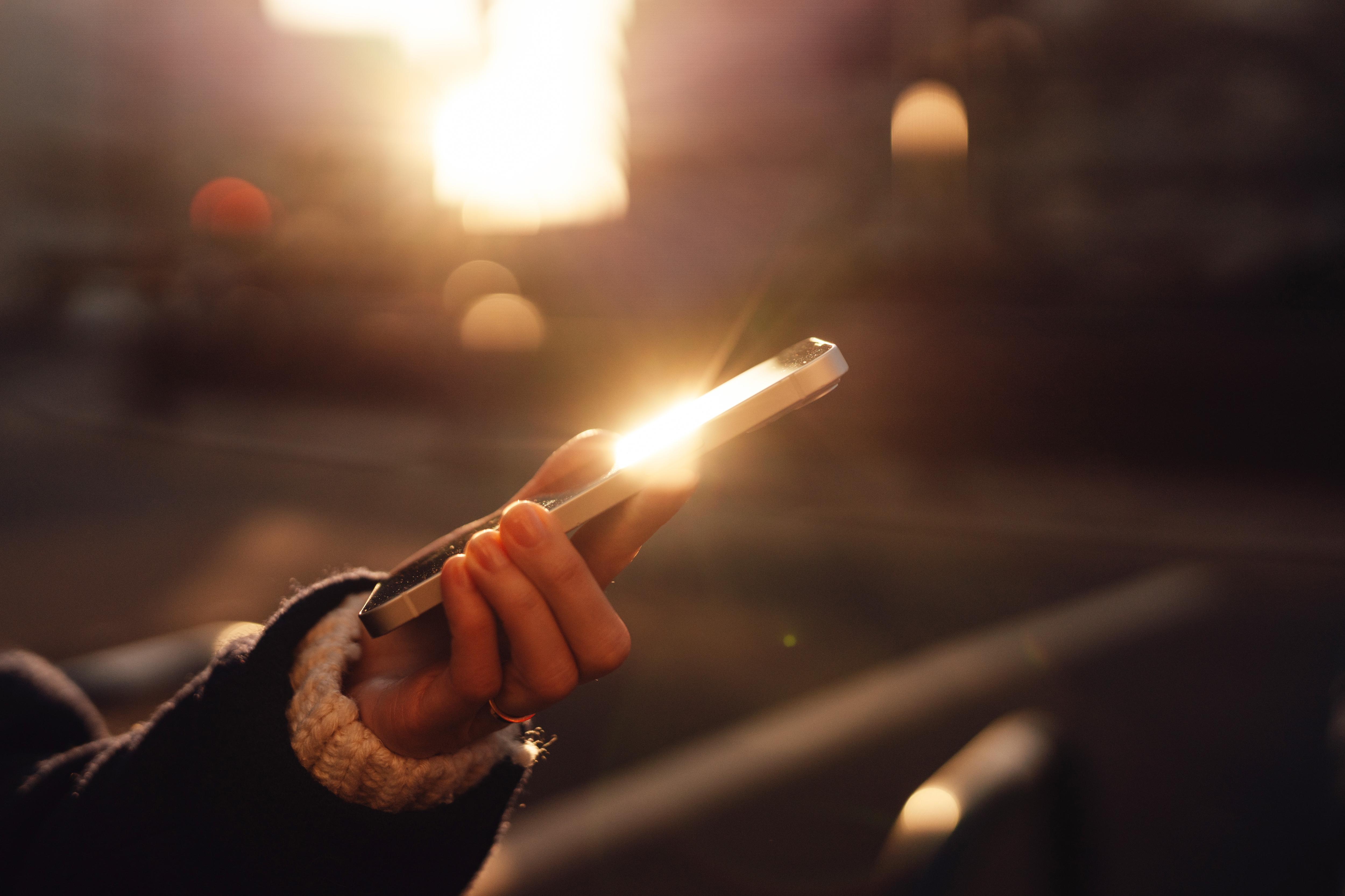 Cropped shot of young woman using mobile app on smartphone in the city at sunset.