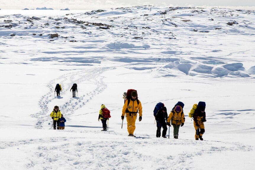 A group of expeditioners walk along the snow.