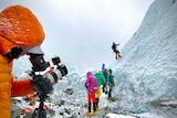 A man films climbers scaling a glacier. 