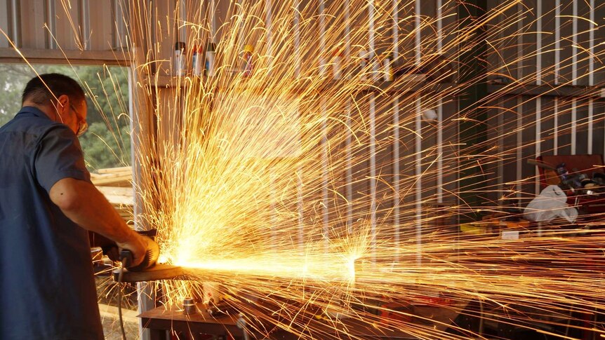 Sparks fly from a grinder in a workshop on a rural property.