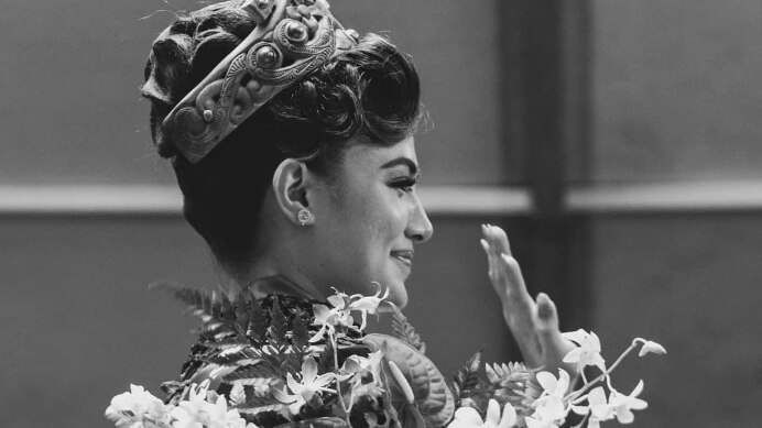 A black and white image of a woman smiling and waving after winning a beauty pageant. 