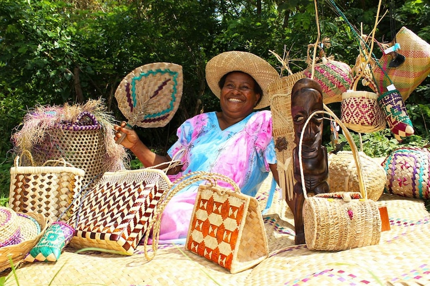 A woman in colourful dress sitting down surrounded by handmade bags.