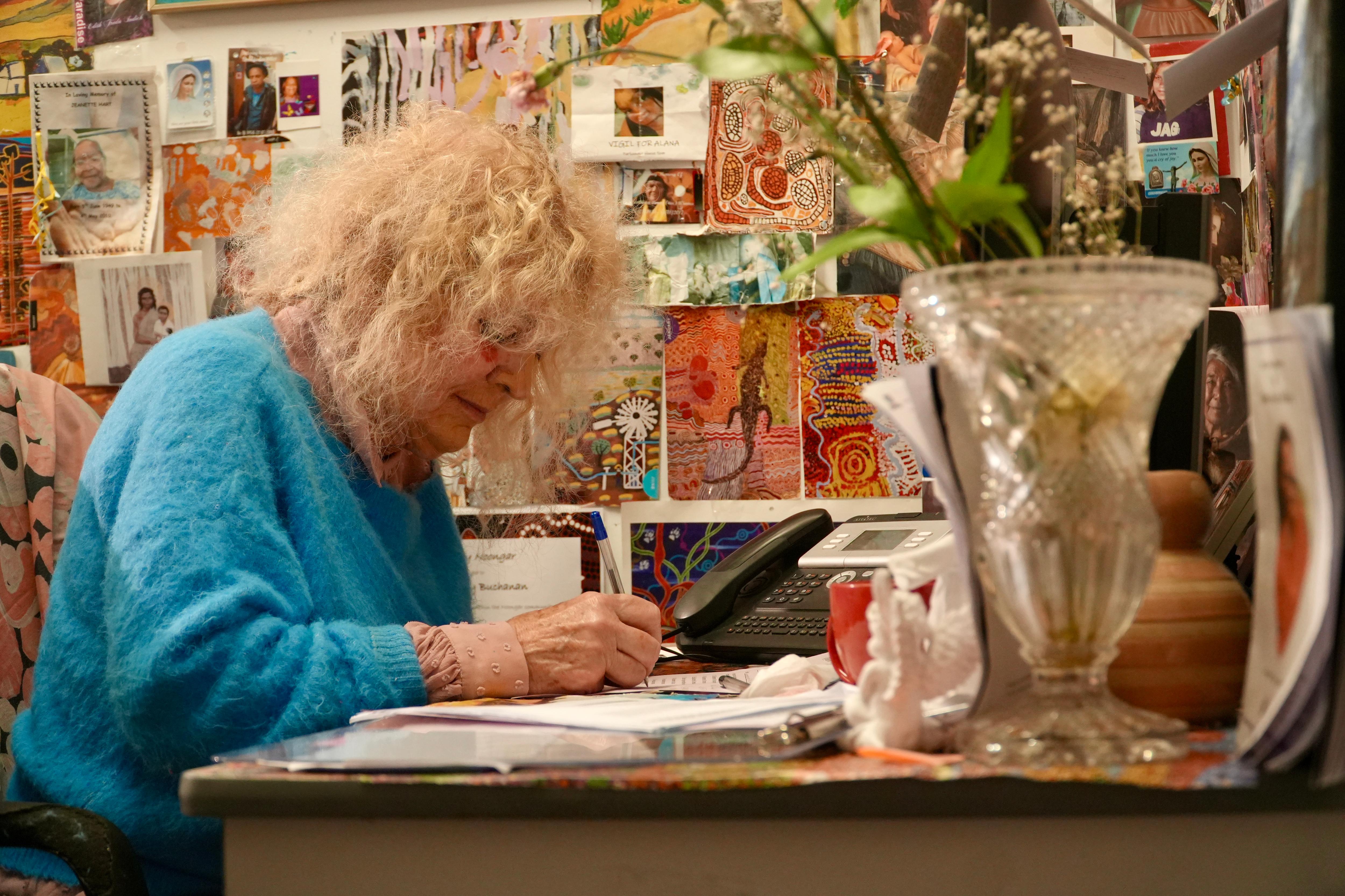 Dr Buchanan sits at a table in a light blue sweater writing.