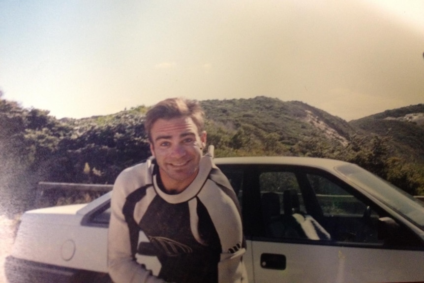 young man smiling in front of camera and car 