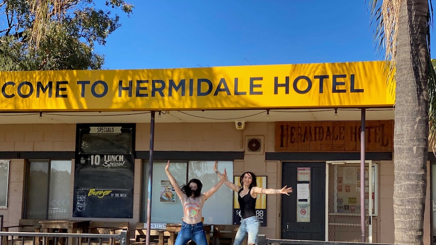 Two people star jump in the air outside the Hermidale Hotel.