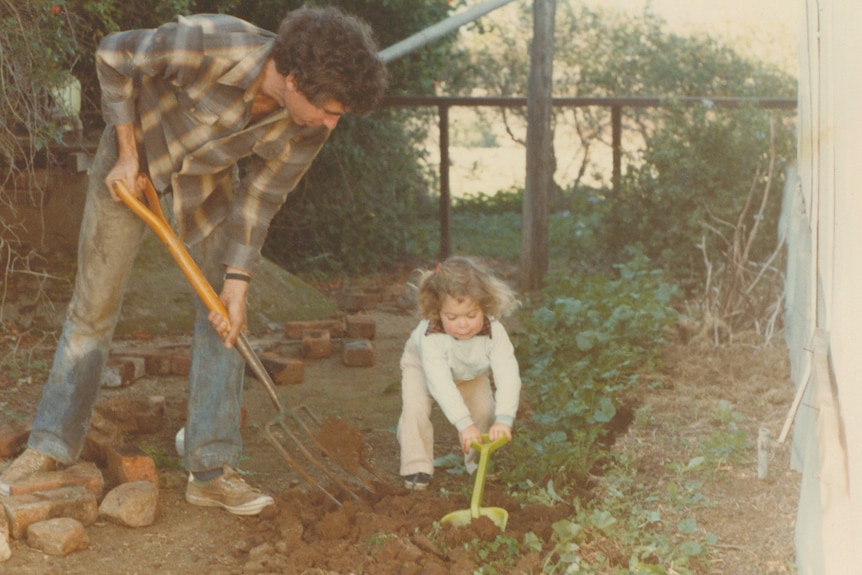 A toddler and a man both have shovels moving dirt in the garden. 