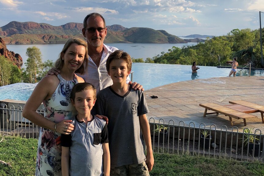 A family standing in front of a pool with mountains in the background.
