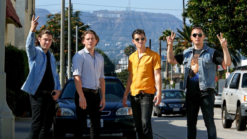 Arctic Monkeys stand on road in classic black jeans and shirts in front of the Hollywood hills