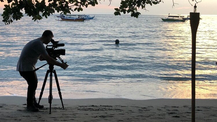 Sunset shot Hemingway standing under a tree filming water.