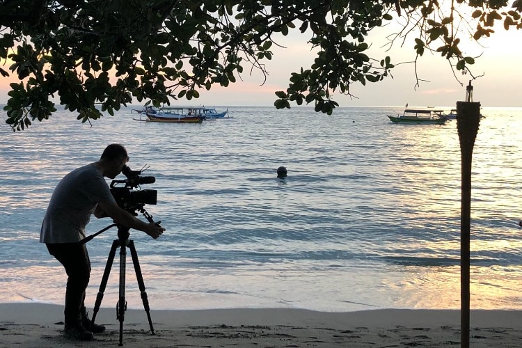 Sunset shot Hemingway standing under a tree filming water.