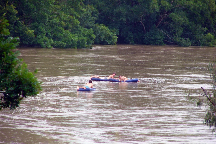 Three boys on airbeds float down a flooded river.