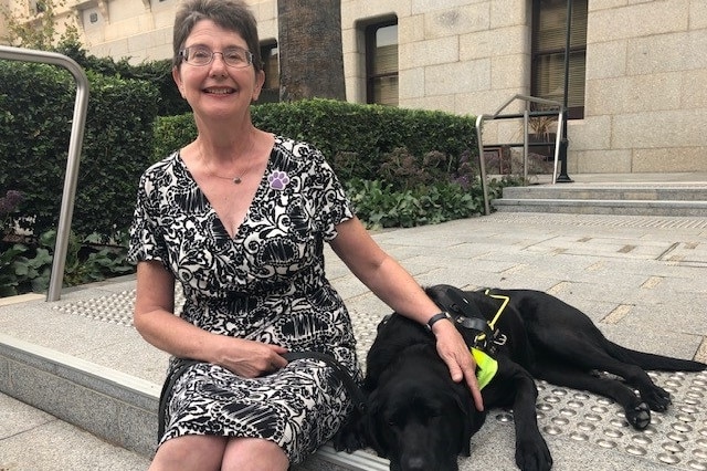 A woman sitting on steps next to her black labrador guide dog