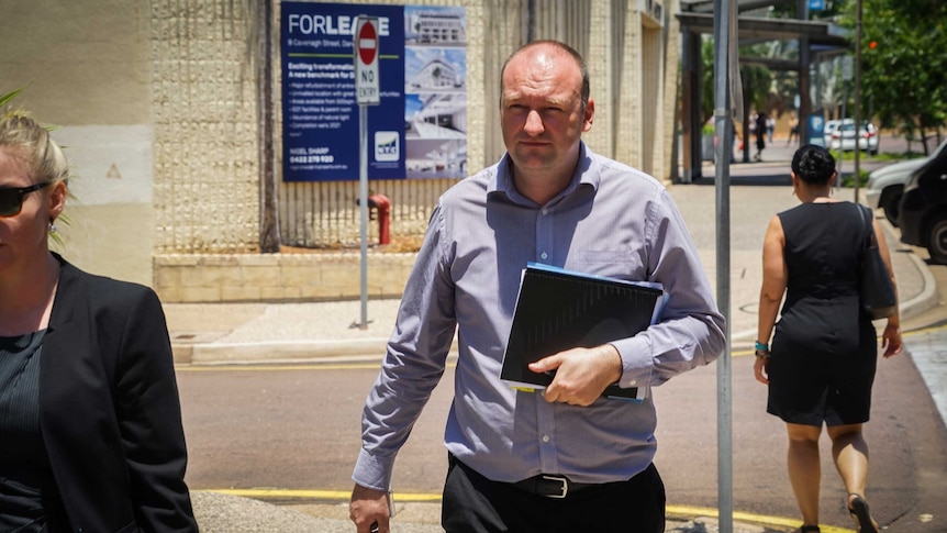 Richard Campion is wearing a blue patterned shirt and leaves Darwin Local Court. He is holding a black folder in his hands.