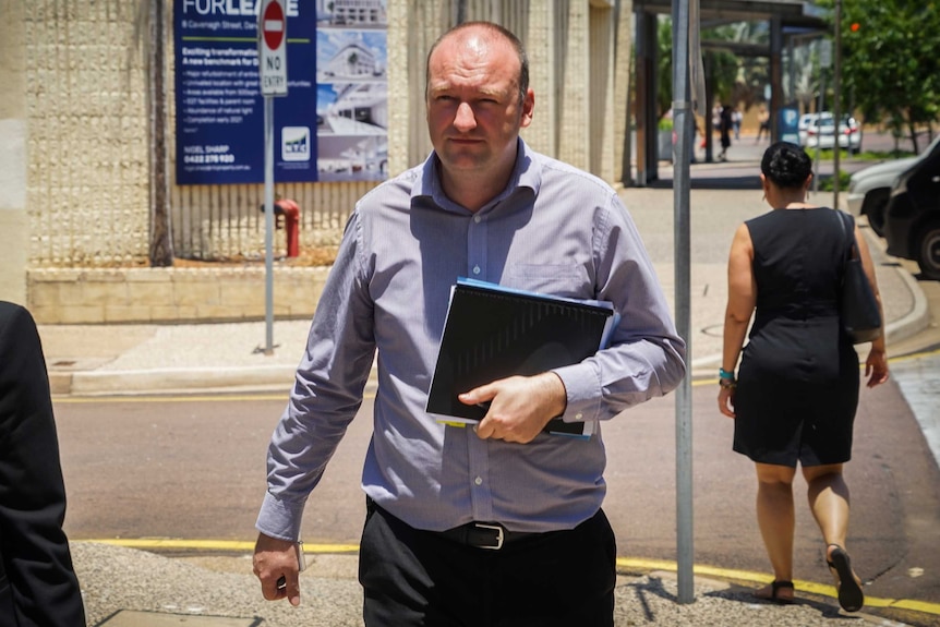 Richard Campion is wearing a blue patterned shirt and leaves Darwin Local Court. He is holding a black folder in his hands.