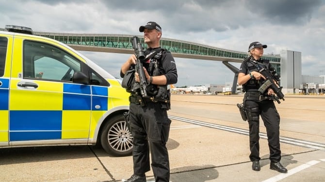 Two police officers standing on an airport runway holding large guns.