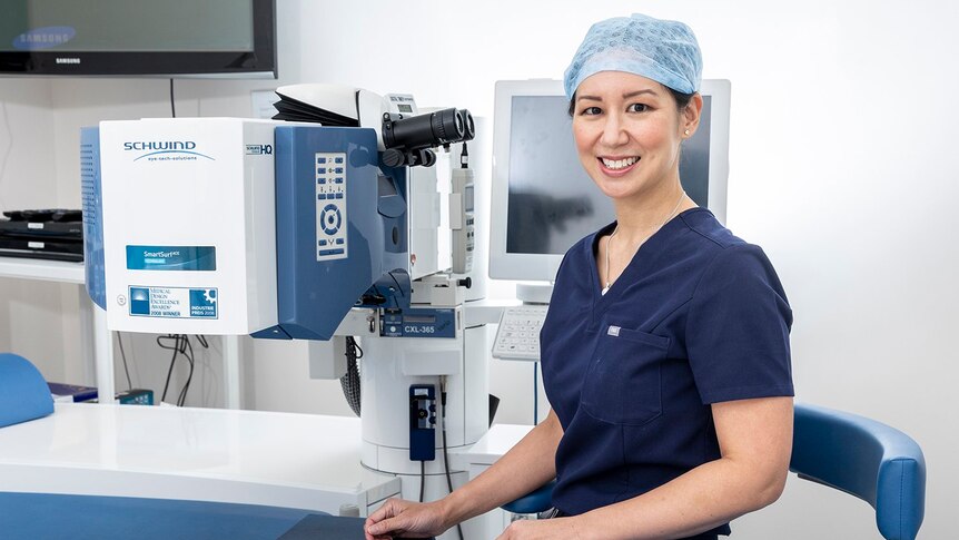 Female doctor in navy scrubs stands in front of eye machine
