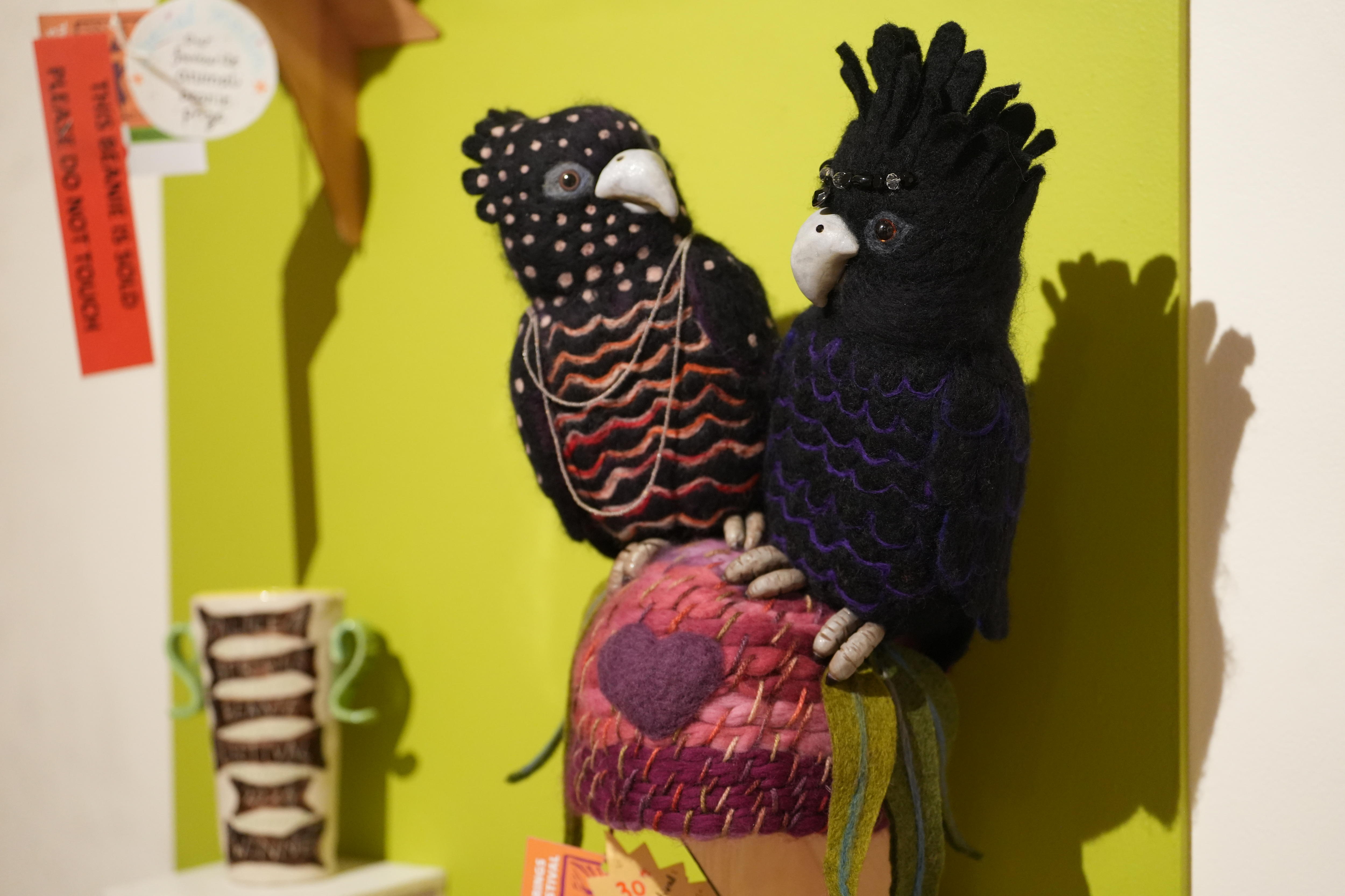A pink felt knit beanie with two large black felted cockatoos on top of the beanie, looking at each other.