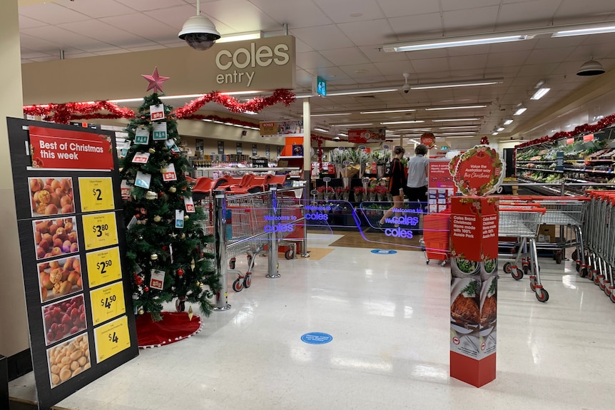The entry to a Coles store with a Christmas tree on left and trolleys on the right.