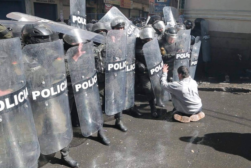 A paraplegic protester kneels before riot police.