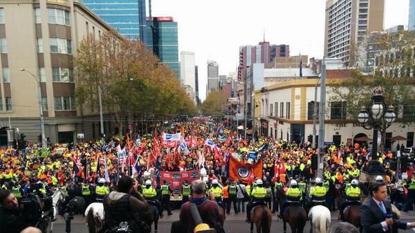 Thousands gather opposite a line of mounted police at state parliament.