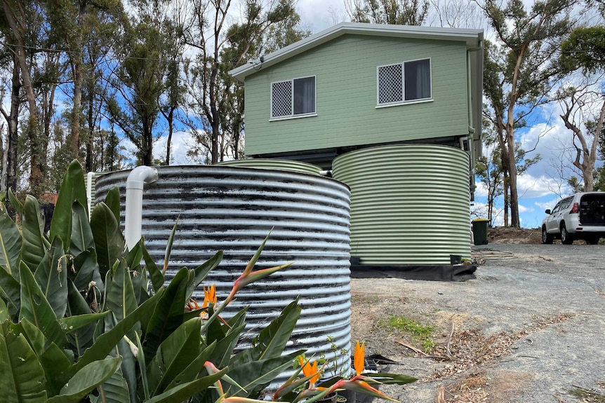 Rainwater tank in foreground with more tanks in front of a new highset home at the top of the incline