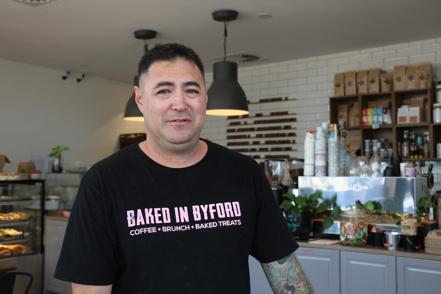 John Russell wears a t-shirt with the words 'baked in Byford' written on the front, with a coffee machine in the background.