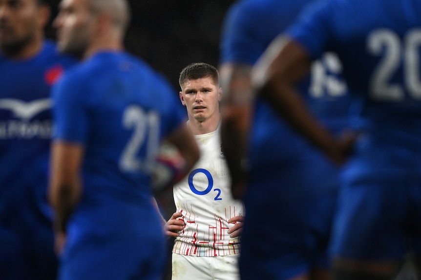 Owen Farrell stands with French players blurred either side in the foreground