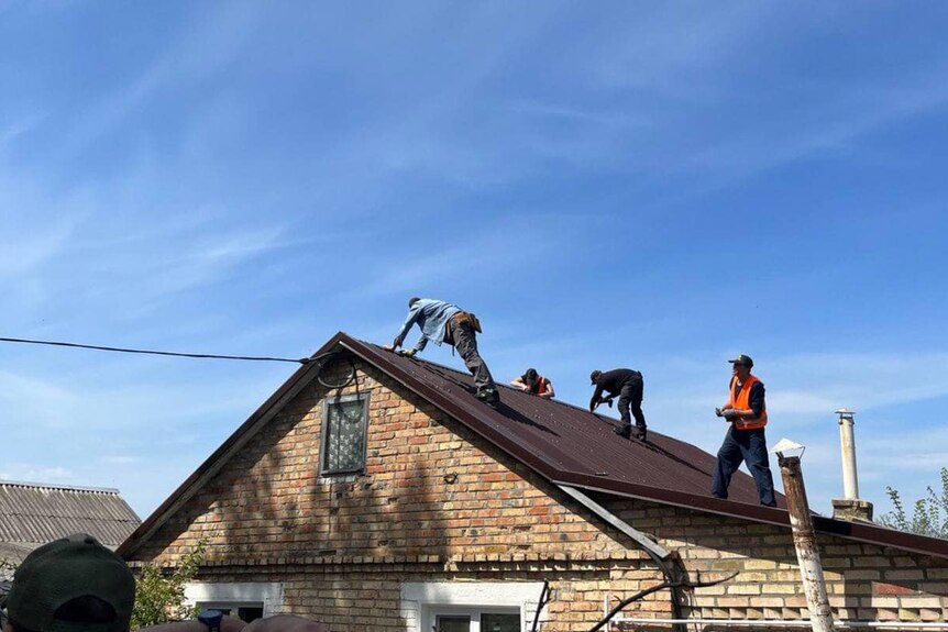 three men stand on a roof of a brick home