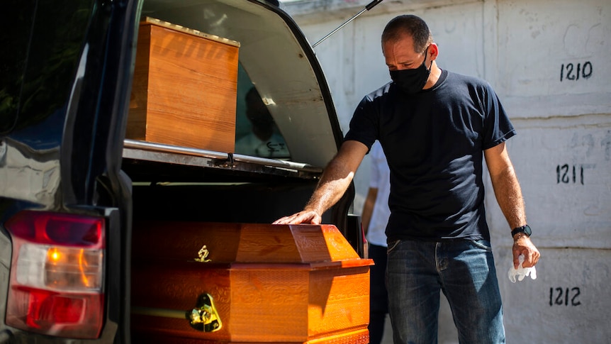 Carlos Alberto places his hand on the coffin belonging to his wife who died from COVID-19 complications.