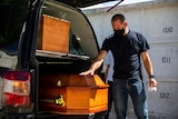 Carlos Alberto places his hand on the coffin belonging to his wife who died from COVID-19 complications.