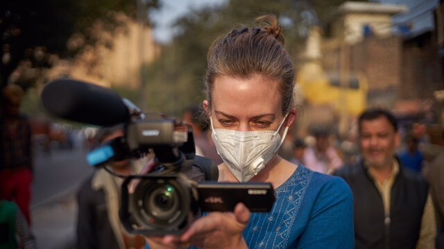 Siobhan Heanue holds a camera while wearing a face mask on a street in India