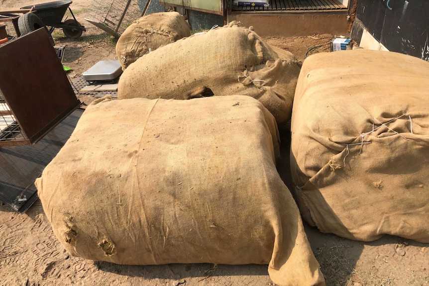 Four full hessian bags lay on a dirt.