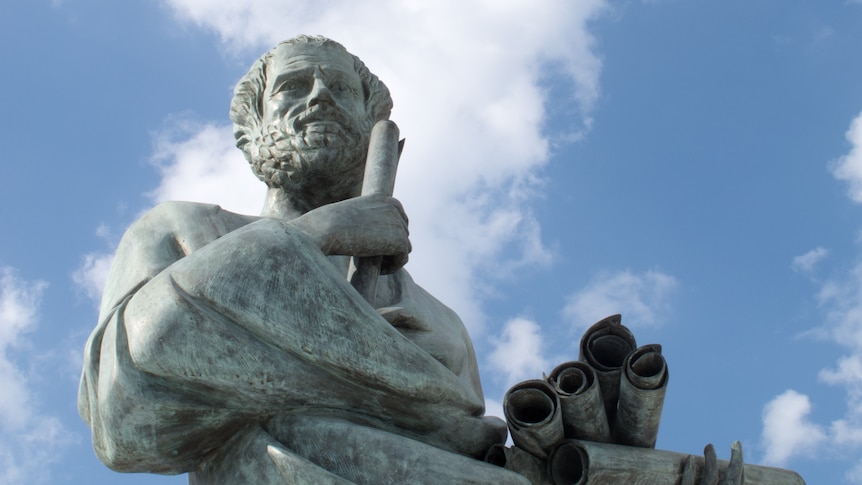 A marble statue of the ancient Greek philosopher Aristotle, viewed from below and set against a cloudy sky