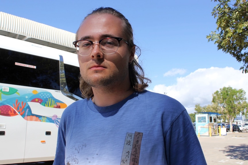 A man in his 20s, fairhaired, in front of a bus.