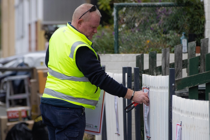 A council worker attaches a notice to a fence.