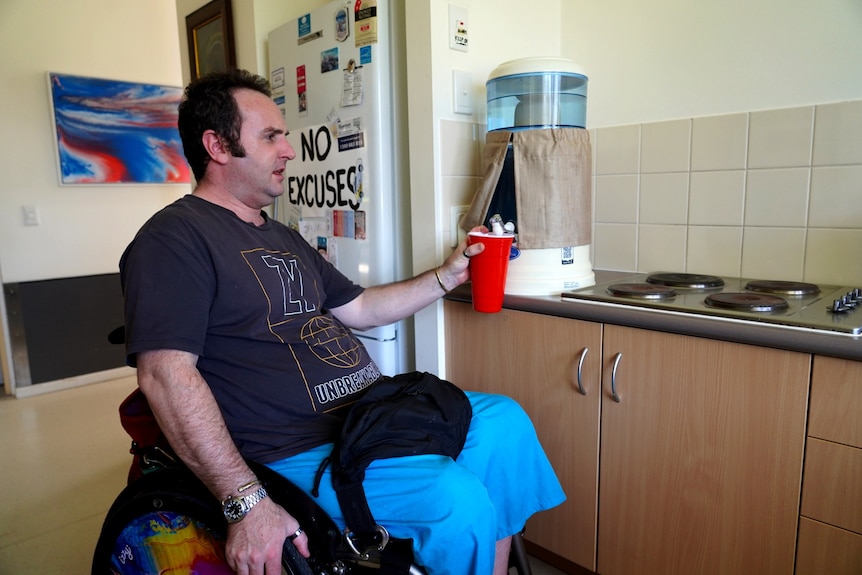 A man in a wheelchair getting a glass of water in his kitchen.
