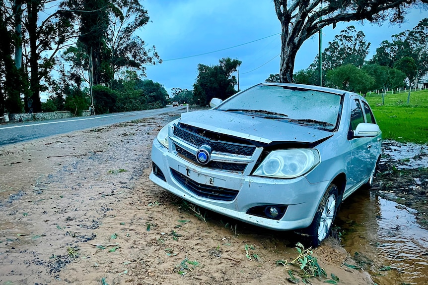 A damaged car sits by the side of a road