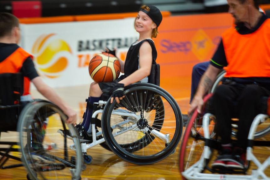 Young wheelchair basketballer navigates between players with a smile