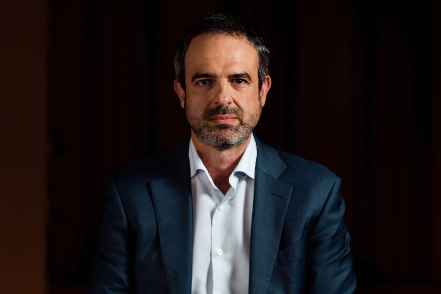 A mid-shot of AMA president Omar Khorshid sitting in a dark room wearing a blue suit and white tie looking at the camera.