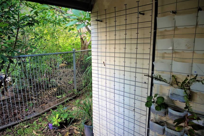 A pool fence is hanging sideways from a bare exterior wall. Part of every third rung is missing.