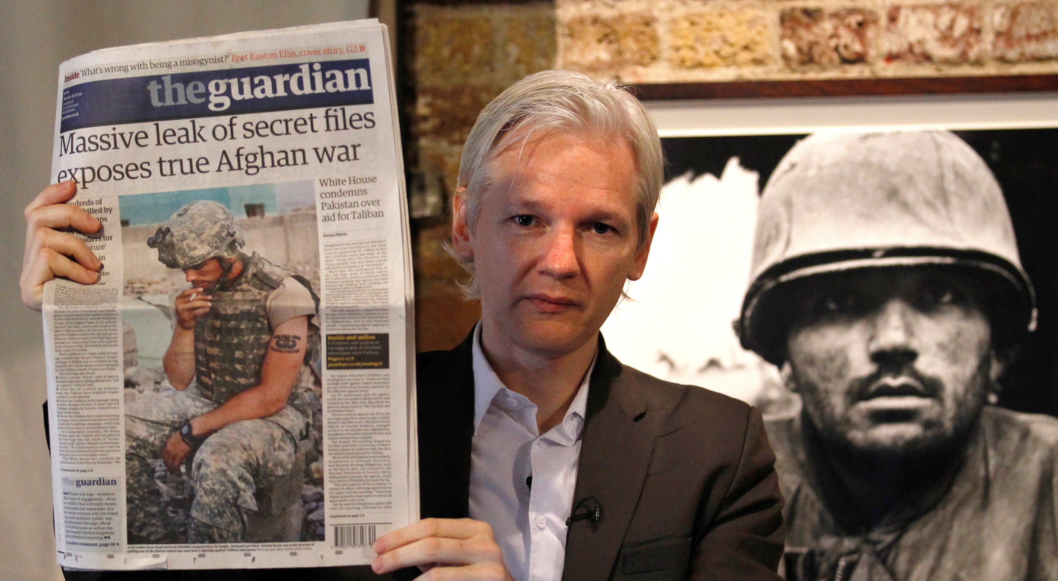 Assange, seen here looking much younger, holds up the newspaper which reads massive leak of secret fules exposes true Afghan war
